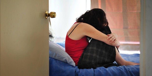 Depressed young woman sitting on the bed at home suffering from a severe depression