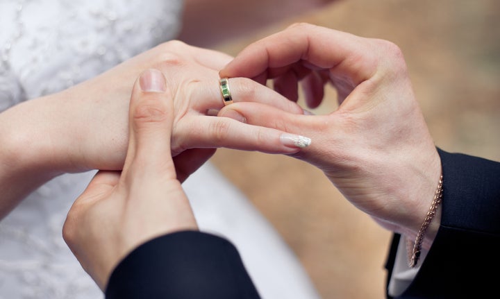 Groom putting a ring on bride's finger during wedding ceremony