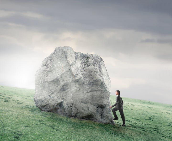 Businessman climbing on a rock on a green meadow