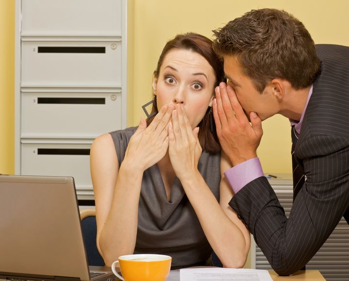 Businessman whispering in businesswoman's ear at office