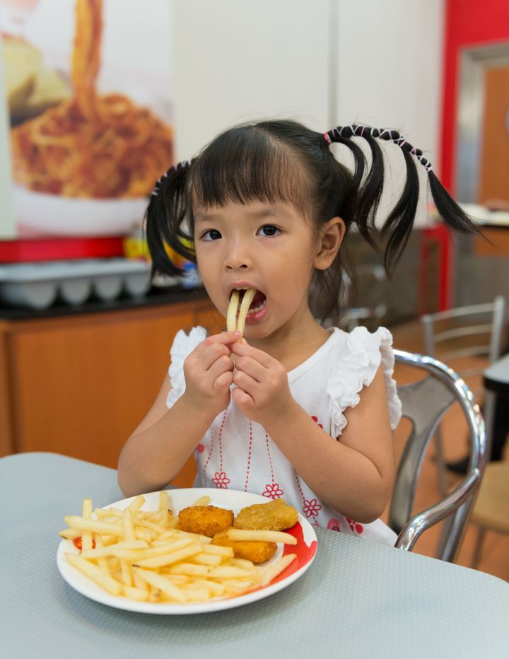 Little girl eating french fries at fast food restaurant