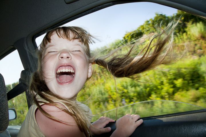 Little fun girl speeds in car near the open window.