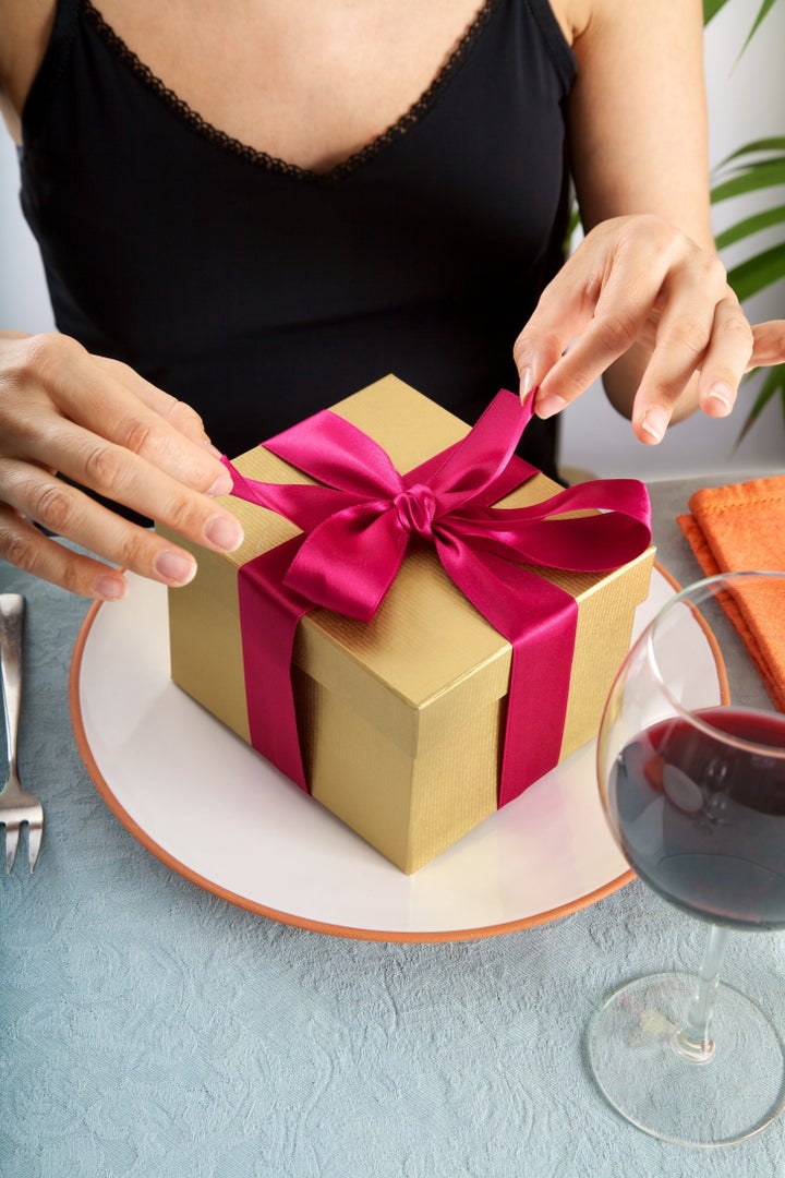 woman at restaurant opening a golden gift package