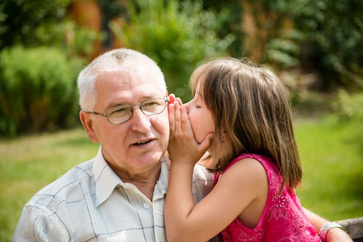 Little girl whispering her grandfather a secret to ear - outdoor in backyard