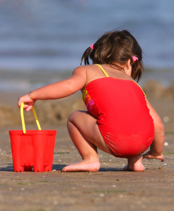 The rear view of a little girl on the beach wearing a red swimsuit.