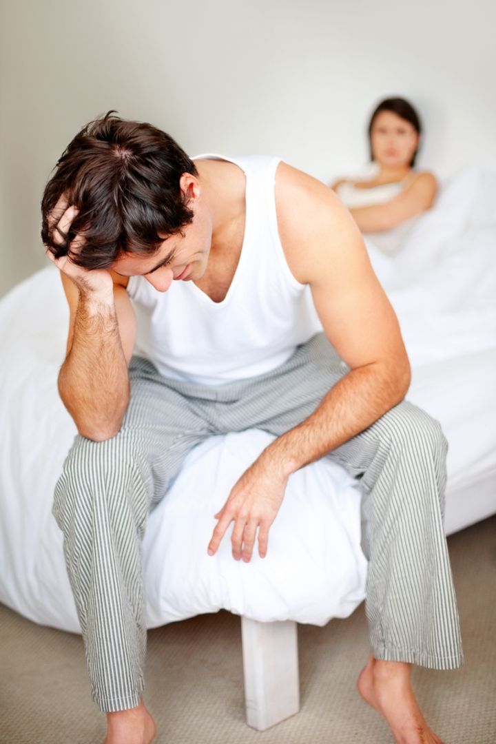 Frustrated young man sitting after having an argument with his wife in bedroom