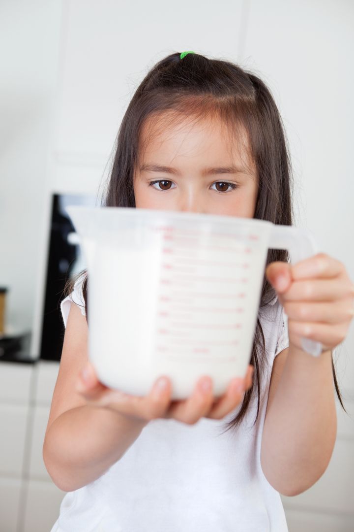 Little cute girl holding milk in a measuring mug