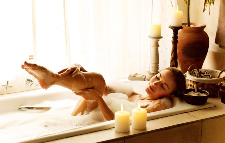 Photo of a woman relaxed at luxury spa salon, picture of young beautiful lady taking bath at home, image of pretty female bathing with soap foam and candles in hotel room, cute girl relax in jacuzzi