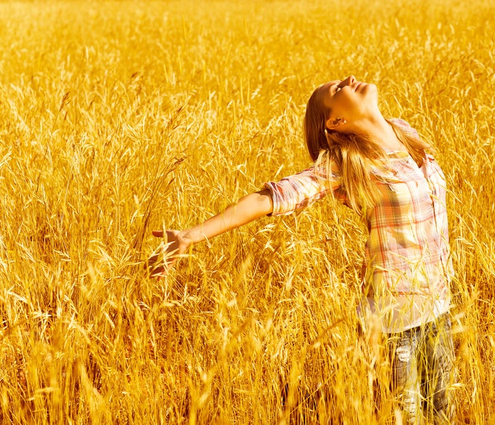 Picture of cheerful teenager having fun in countryside, cute happy female standing on wheat field with raised open hands and looking up, blond girl enjoying autumn nature, fall season