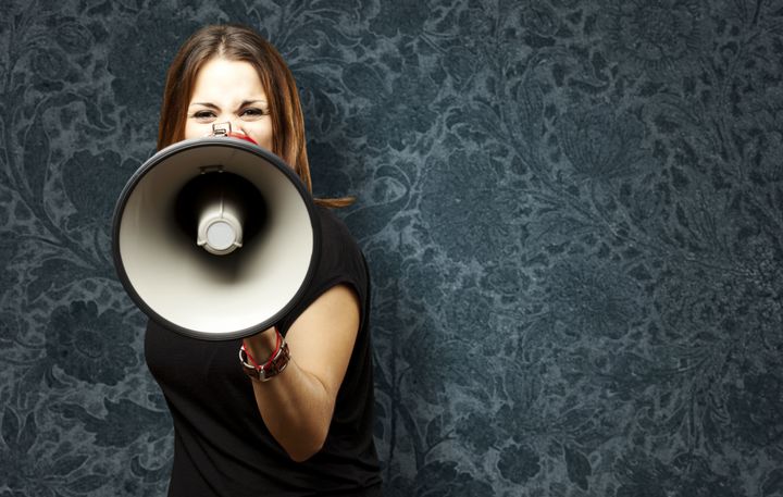 portrait of young woman shouting with megaphone against a vintage wall