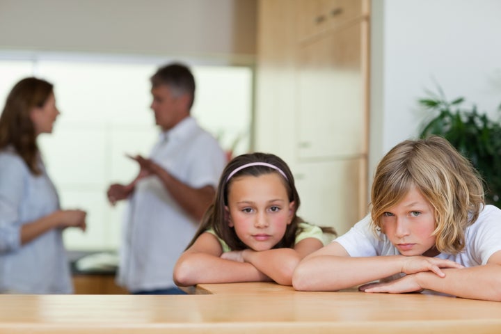 Sad looking siblings with their fighting parents behind them