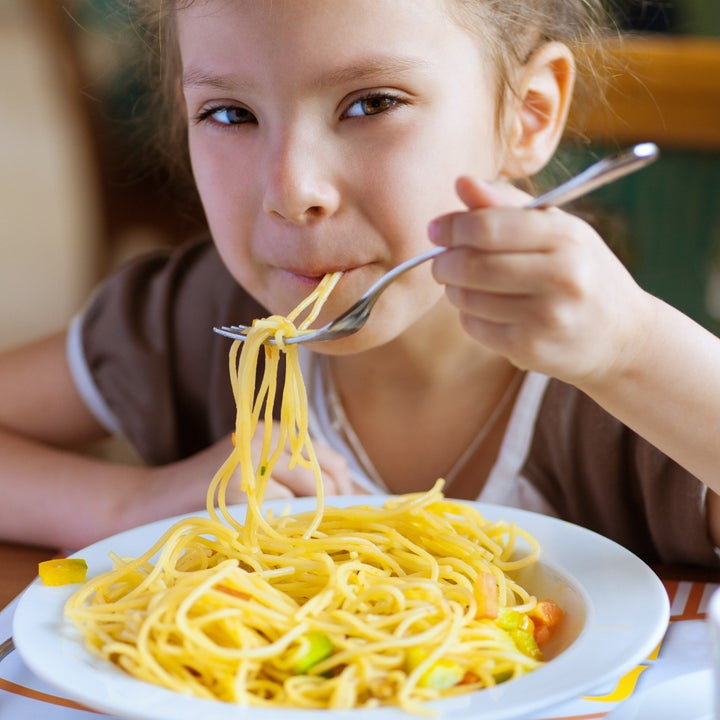 Small girl eating spaghetti with fork and smiles.