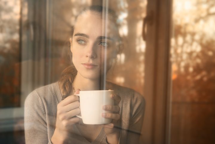 beautiful woman drinking coffee in the morning sitting by the window. view from outside.