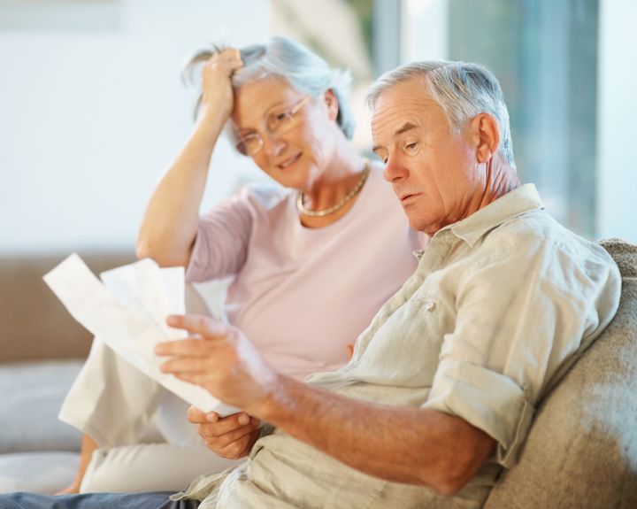 Elderly man with his wife going through documents on couch , worried about savings