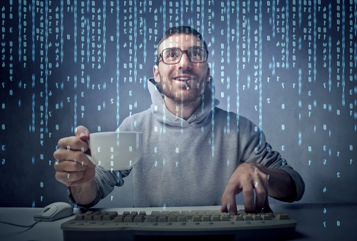 Smiling man sitting in front of a computer screen and holding a cup of coffee