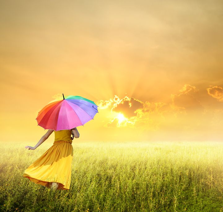 Beautiful woman holding multicolored umbrella in green grass field and sunset