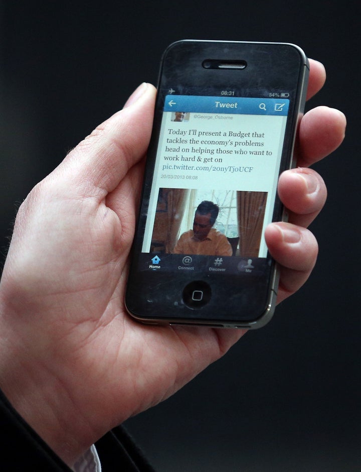 LONDON, ENGLAND - MARCH 20: A reporter reads a pre-budget tweet from George Osbourne in Downing Street ahead of the annual budget being presented to Parliament at 11 Downing Street on March 20, 2013 in London, England. The Chancellor, under pressure after the UK lost its AAA credit rating last month and the lack of growth in the economy, is predicted to reveal plans to continue with his austerity strategy to cut the UK's deficit. It is likely that Mr. Osborne will announce further spending cuts to Whitehall departments with the savings put in place to boost large scale infrastructure projects, with both tax breaks on childcare and a rise in fuel duty also high on the agenda. (Photo by Matt Cardy/Getty Images)