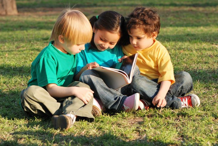 Group of children with the book on a grass in park