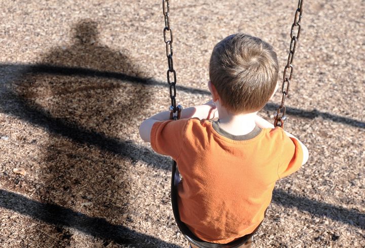 A young boy is sitting on a swing set and looking at a shadow figure of a man or bully at a playground. Use it for a kidnap, defense or safety concept.