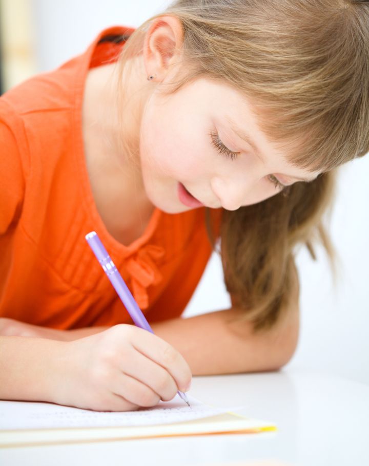 Cute little girl is writing using a pen in preschool
