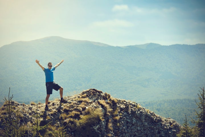 free man on mountain rock with arms raised.