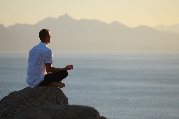 Guy sitting on a rock in the lotus position and looking at the setting sun