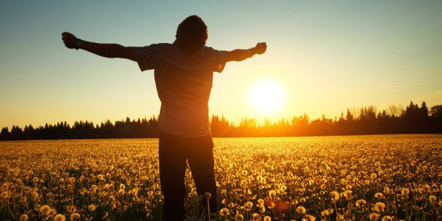 Young man standing on a meadow with dandelions on sunset sky background