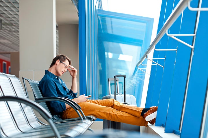 Young adult man waiting for his flight at the airport lounge and using a smart phone.