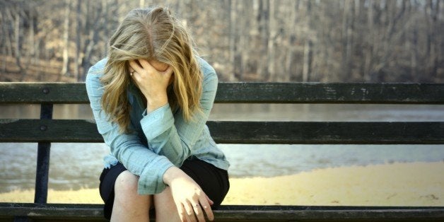 very sad blonde girl holding her head on a bench