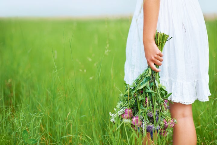 Cropped image of a woman holding flowers behind her back while walking in a field