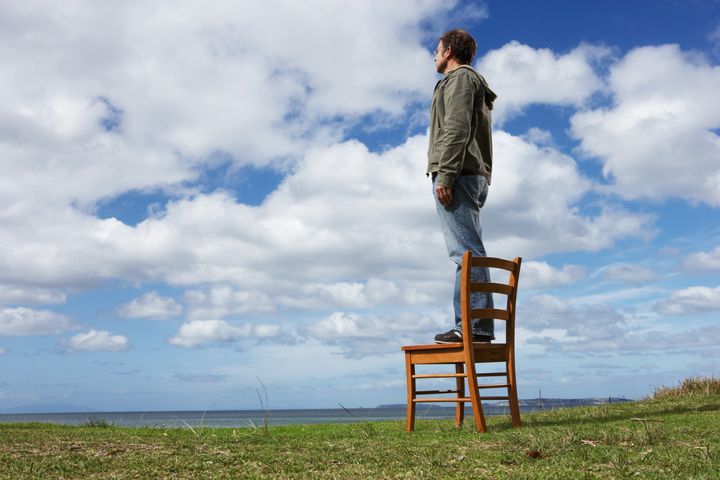 Man standing on chair in field, looking at landscape, side view