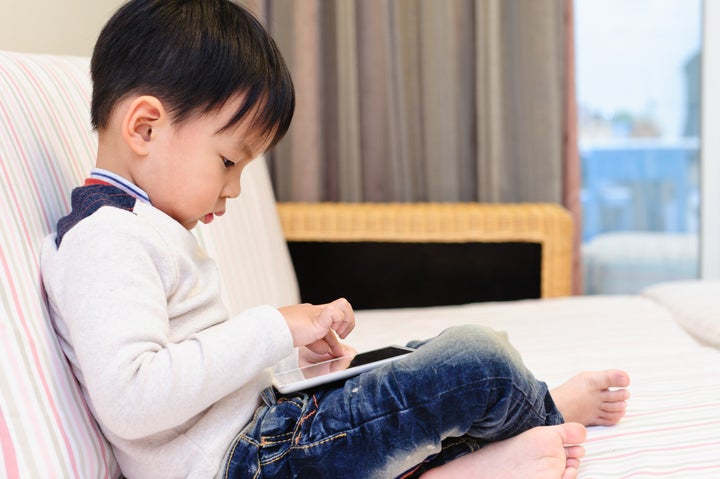 The little boy in the living room on the sofa using digital tablet to play games.