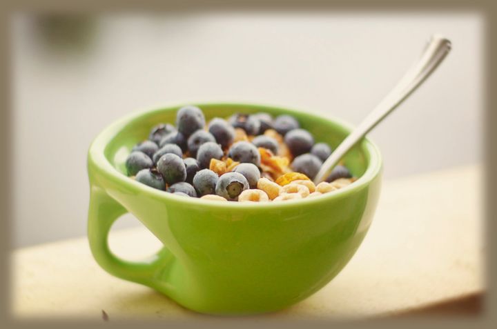 Close-up of green bowl in cereal and blueberries with spoon.