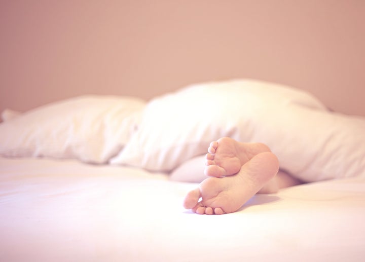 The soles of a women's feet as she lays in her bed.