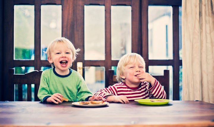 Two happy smiling little brothers sat at breakfast table eating toast.