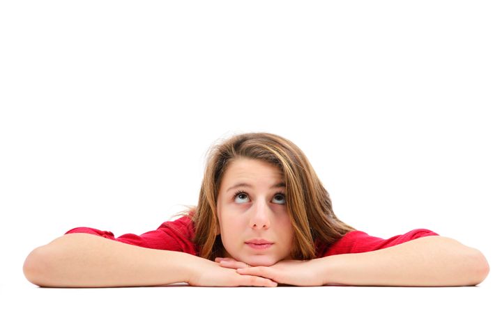 Young girl with long brown hair laying on the floor while looking up. Isolated on white. Much copy space.