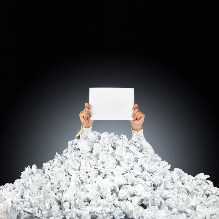 Person under crumpled pile of papers with hand holding a help sign