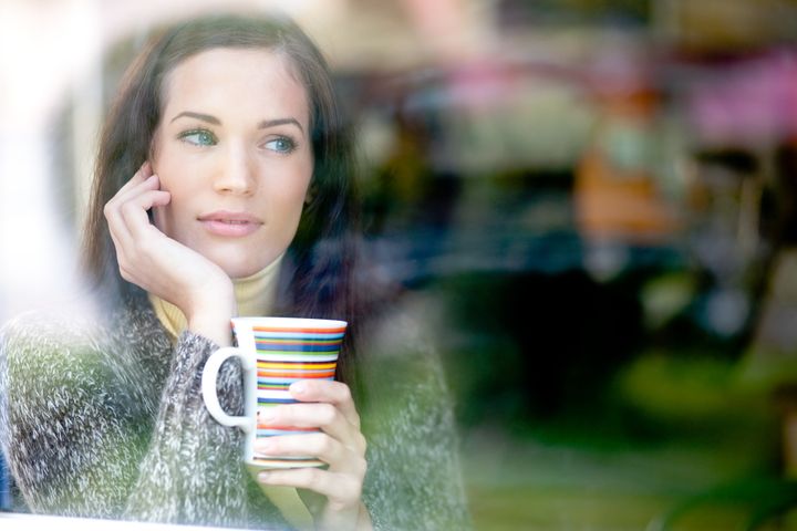 Winter portrait of a young woman looking out the window enjoying a hot cup of tea / coffee