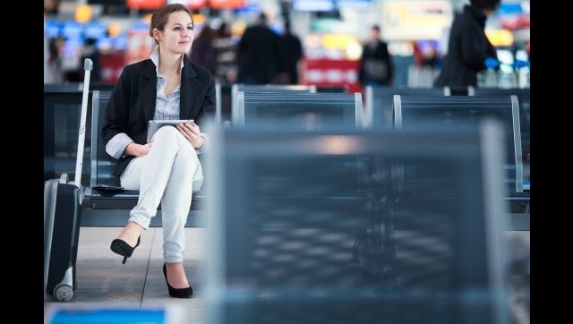 Young female passenger at the airport, using her tablet computer while waiting for her flight (color toned image)