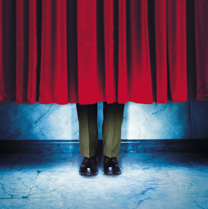 Legs of a man in military uniform hiding behind a red velvet curtain. Stalin had the curtains in the Kremlin raised so no one could hide behind them.