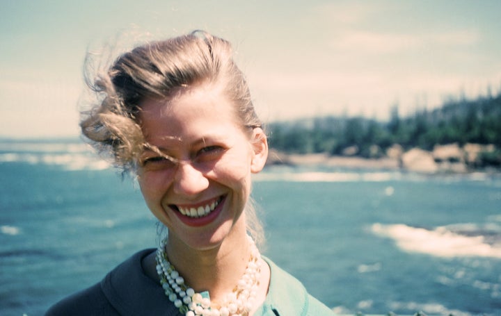 Woman poses in front of the ocean, her hair falling over one eye, wearing her trousseau of chic fitted blazer and fashionable faux pearl necklace.