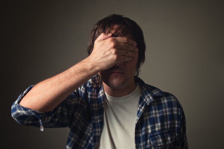 Ashamed man covering his eyes with hand, casual clothing, low light. Face palm, shame, problem, trouble, ignorance concept.