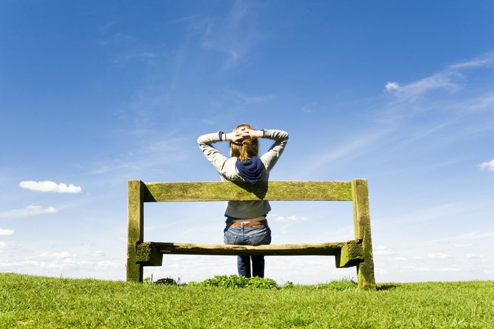 Young Woman Relaxing On A Park Bench On A Clear Summers Day