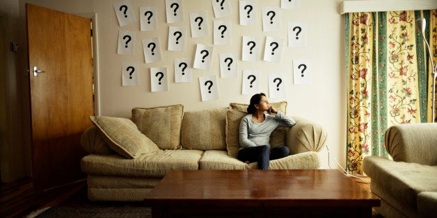 Woman sitting on sofa with question marks on wall.