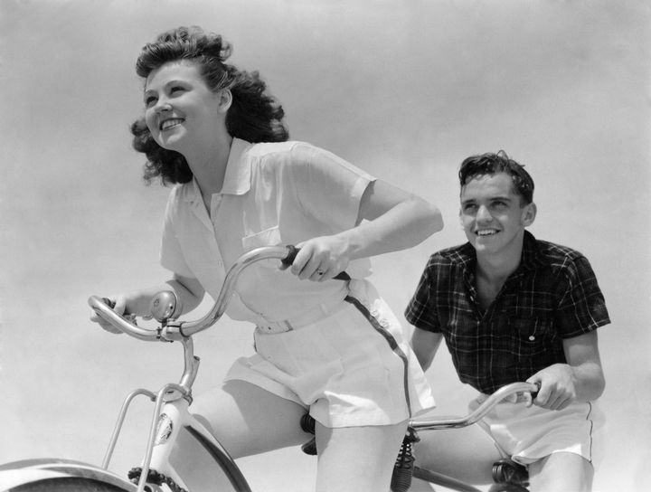 UNITED STATES - CIRCA 1930s 1940s: Smiling, Eager Teen Couple (Boy And Girl) Grip Handlebars While Riding Bike. Both Are Wearing White Shorts, The Girl Has A White Blouse And The Boy Wears A Dark Shirt. (Photo by H. Armstrong Roberts/Retrofile/Getty Imag