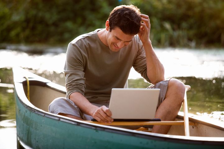 Young man sitting in a boat working on a laptop
