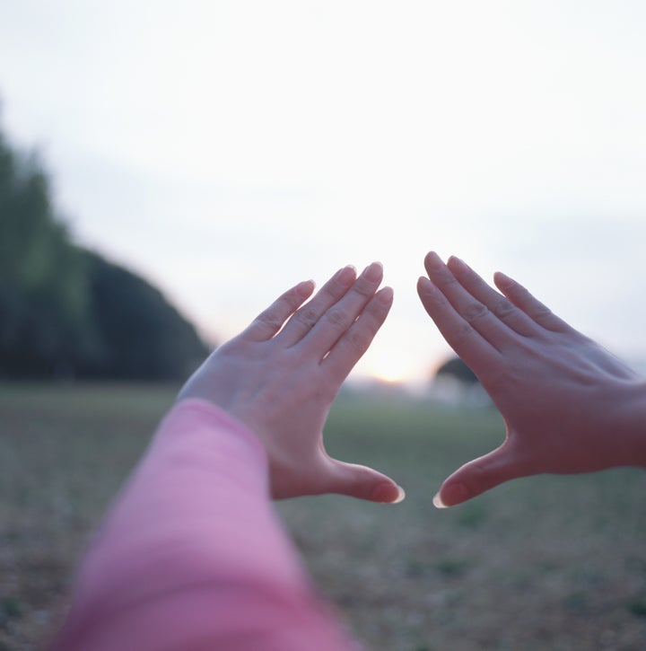 Young woman framing sun with hands (focus on hands)