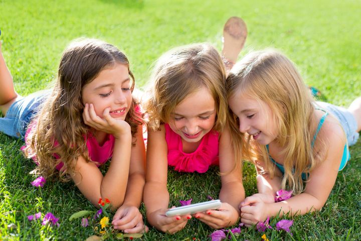 children friend girls group playing internet with mobile smartphone on grass