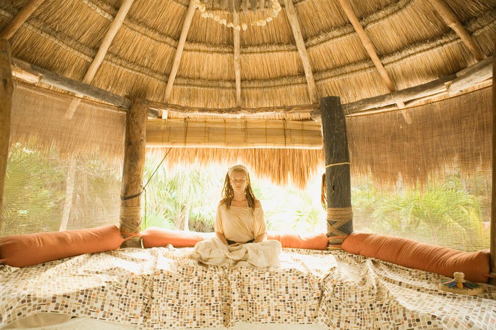 Young woman meditating on bed in hut