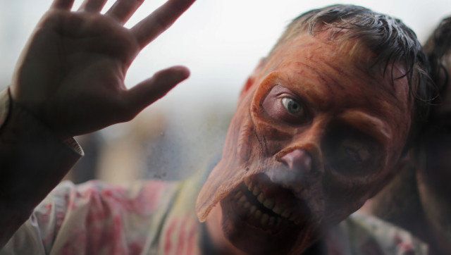 TELFORD, ENGLAND - FEBRUARY 16: An enthusiast dressed up as a Zombie pushes himself towards a window during the MCM Midlands Comic Con Expo at The International Centre on February 16, 2013 in Telford, England. Enthusiasts at the Comic Convention are encouraged to wear a costume of their favourite comic character and flock to the Expo to gather all the latest news in the world of comics, manga, anime, film, cosplay, games and cult fiction. (Photo by Christopher Furlong/Getty Images)